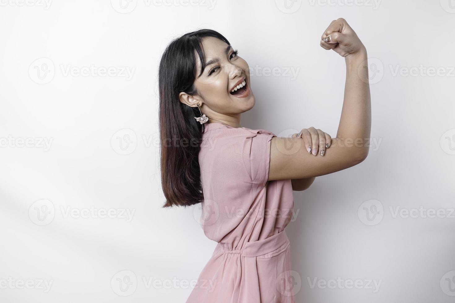 upphetsad asiatisk kvinna bär en rosa blus som visar stark gest förbi lyft henne vapen och muskler leende stolt foto