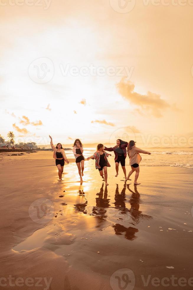 en grupp av asiatisk tonåringar löpning med Lycklig uttryck på semester med deras vänner full på de strand foto