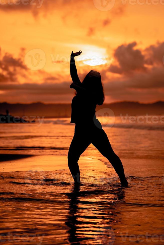 silhuett bild av ett asiatisk kvinna håller på med balett rörelser mycket flexibelt på de strand foto