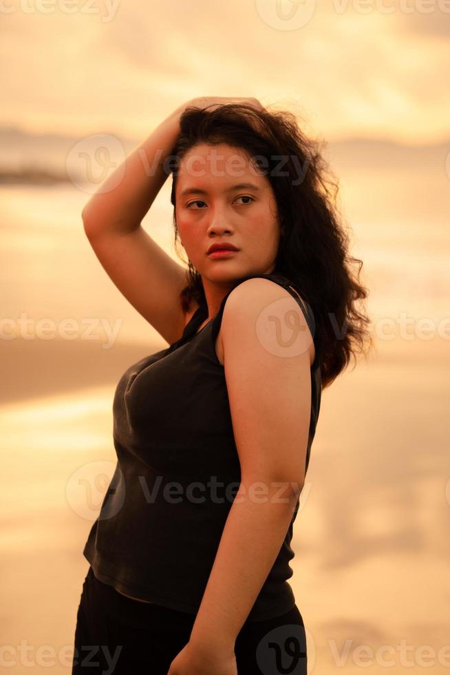ett asiatisk kvinna Framställ med henne händer Uppfostrad och rörande henne svart hår passionerat på de strand foto