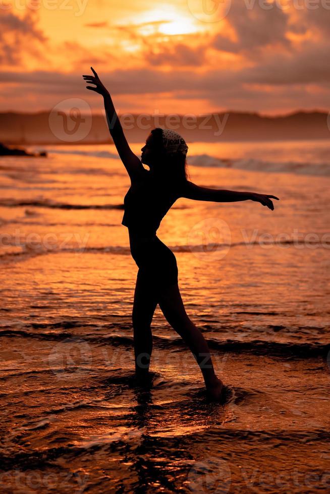 silhuett av en mycket smal ballerina håller på med balett öva ensam på de havsstrand med vågor kraschar på henne foto