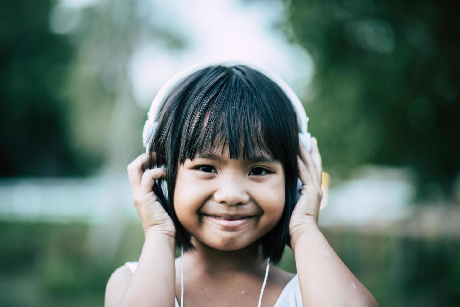 liten flicka som lyssnar på musik i parken med hörlurar foto