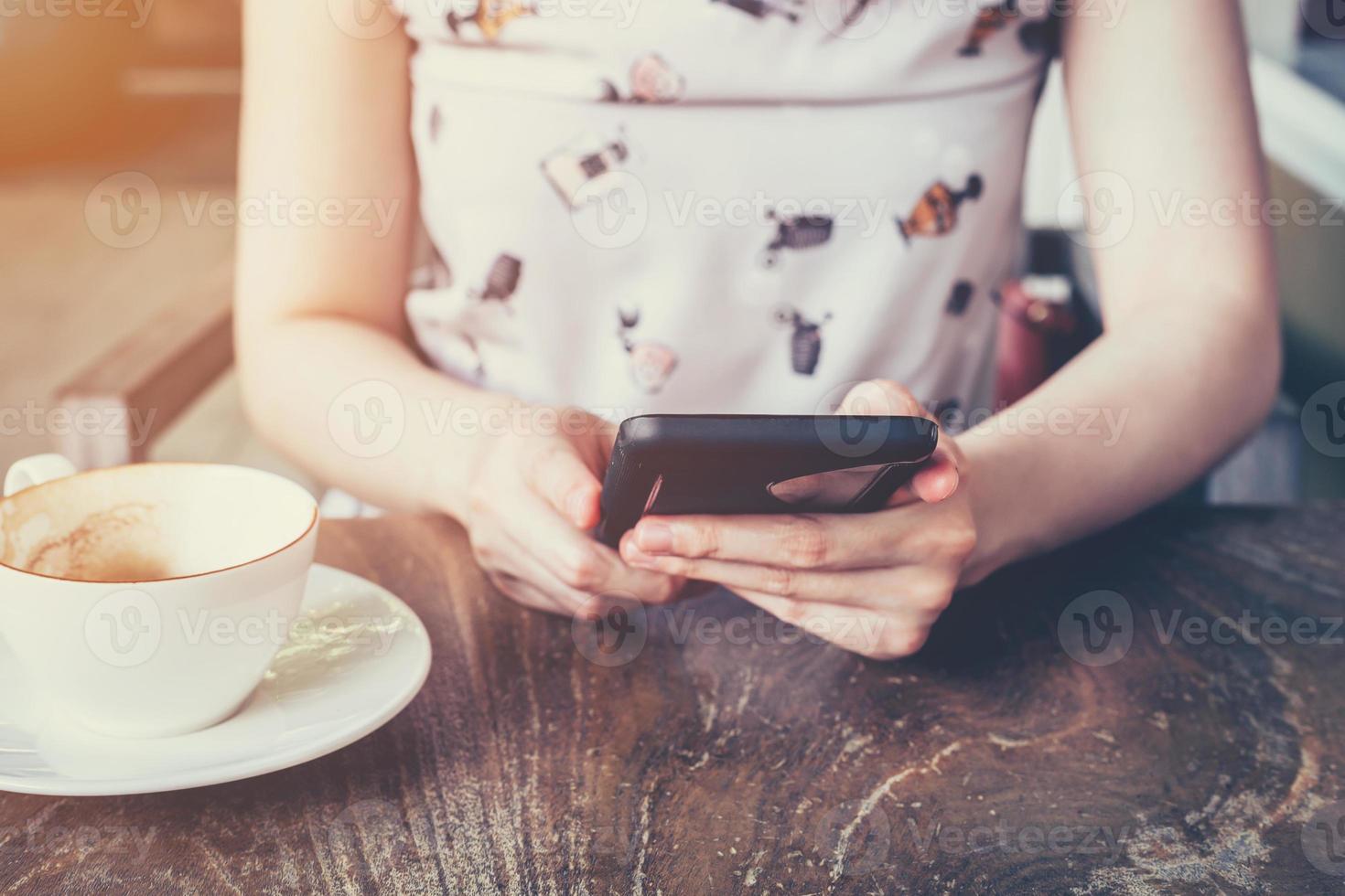 stänga upp av hand kvinna använder sig av telefon i kaffe affär med djup av fält, årgång tonad. foto