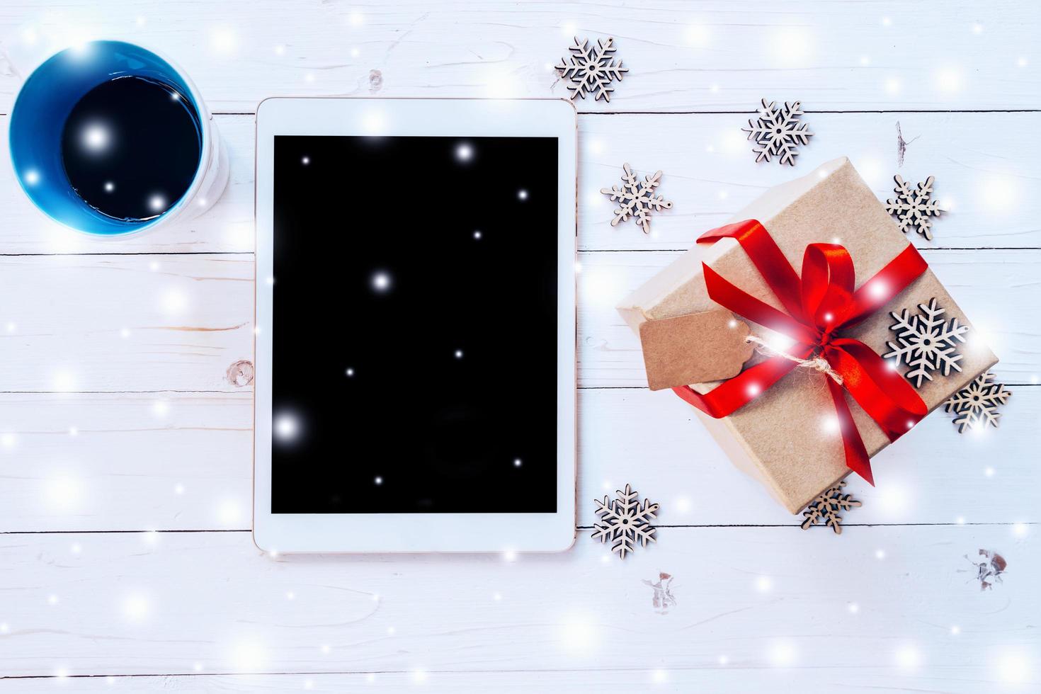 topp se läsplatta, kaffe kopp och gåva låda med snö och snöflingor på vit trä bakgrund för jul och ny år. foto