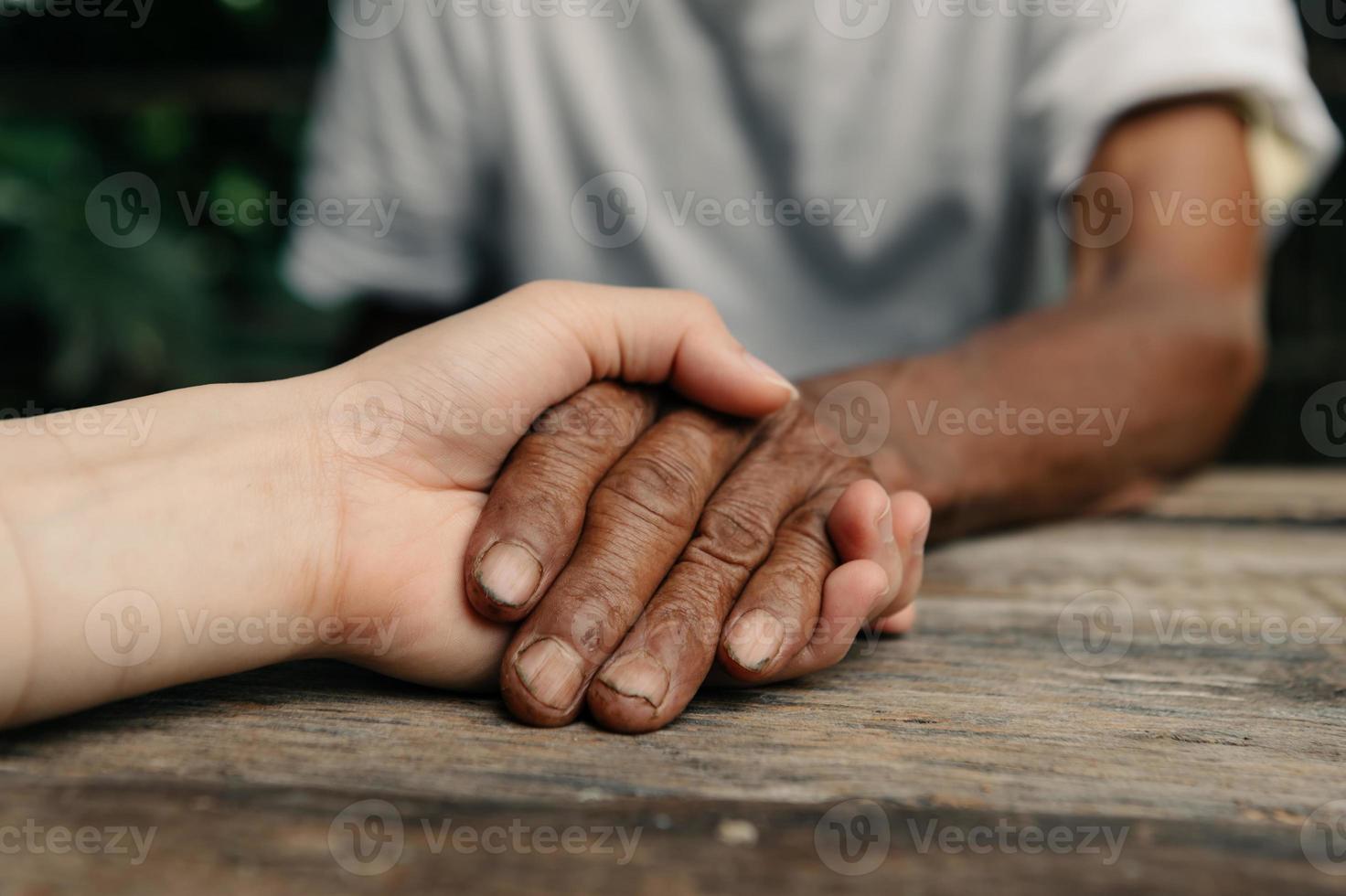 händer av de gammal man och en kvinna hand på de trä tabell i Sol ljus foto