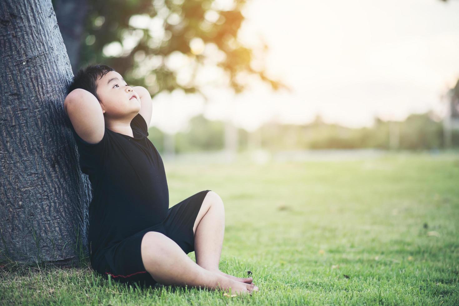 liten pojke som sitter under trädet och tänker foto