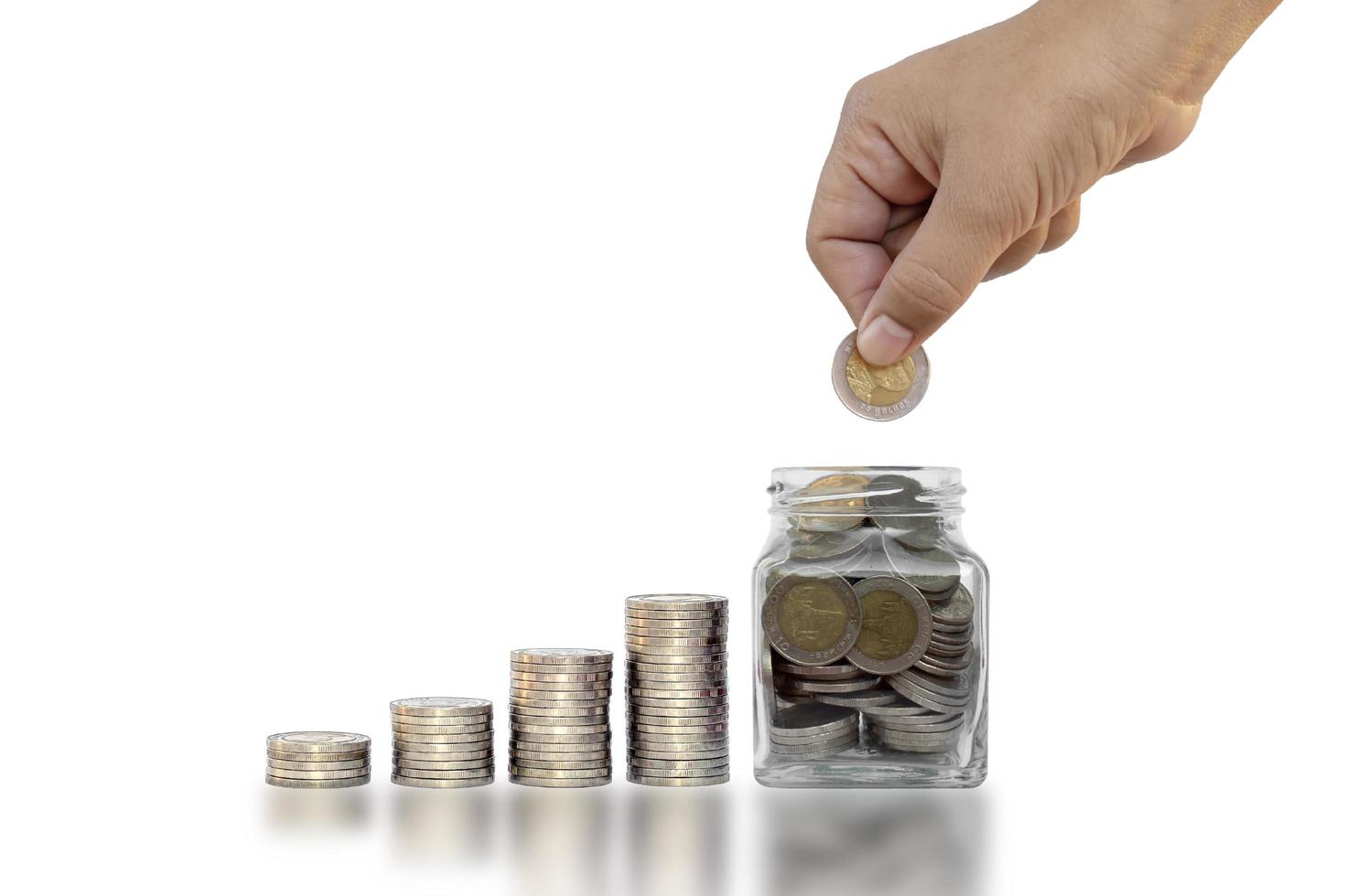 hand som håller ett mynt i en pengarsparande flaska på en vit bakgrund foto