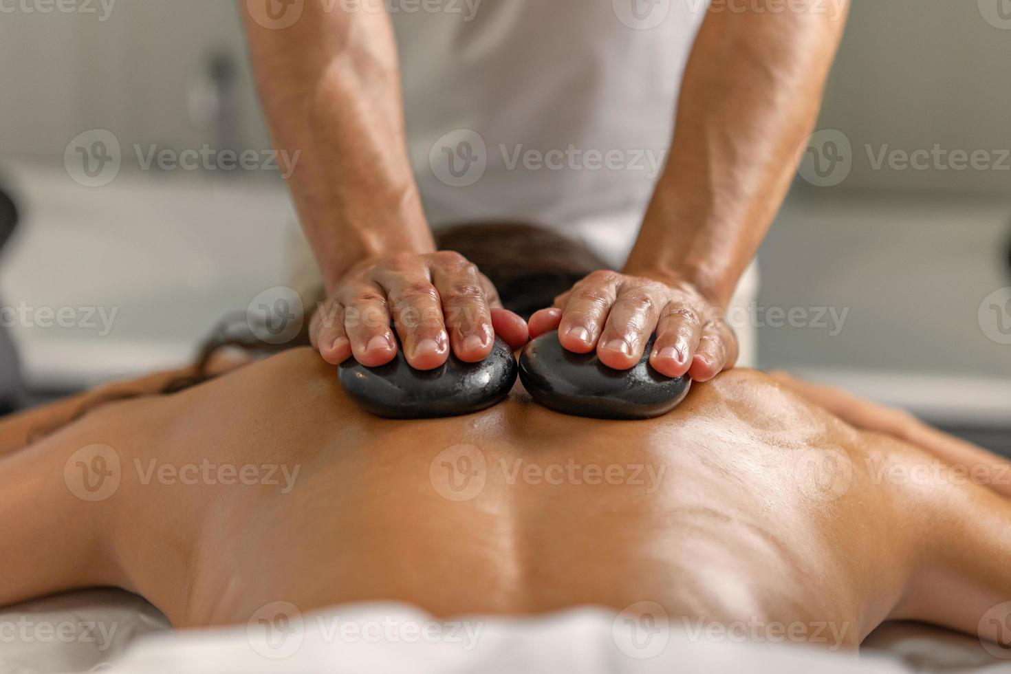 stänga bak- se av kvinna har tillbaka massage med stenar förbi professionell massör i hälsa spa foto