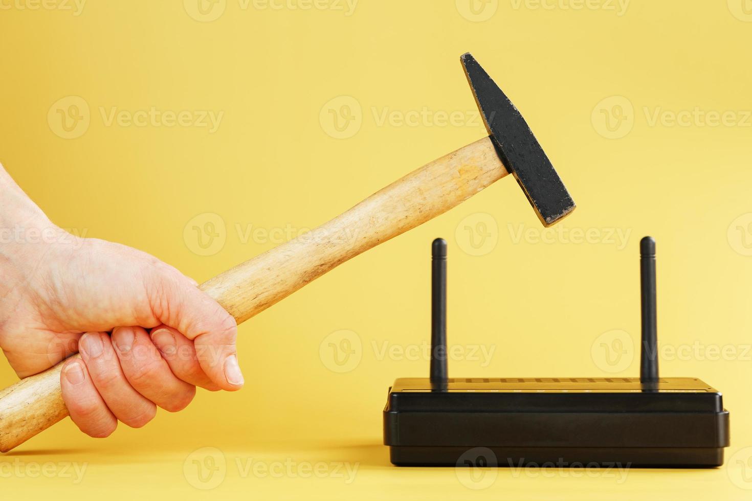 en hammare träffar de Wi-Fi modem router till ha sönder den mot en gul bakgrund. foto
