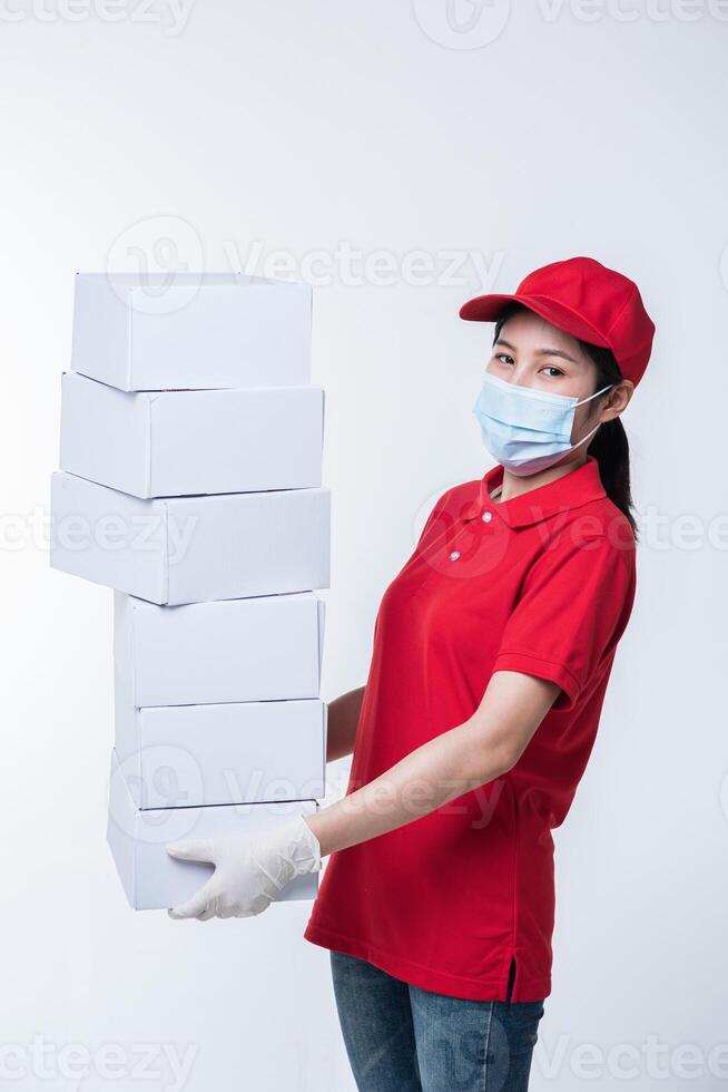 bild av en medveten ung leverans man i röd keps tom t-shirt enhetlig ansikte mask handskar stående med tömma vit kartong låda isolerat på ljus grå bakgrund studio foto