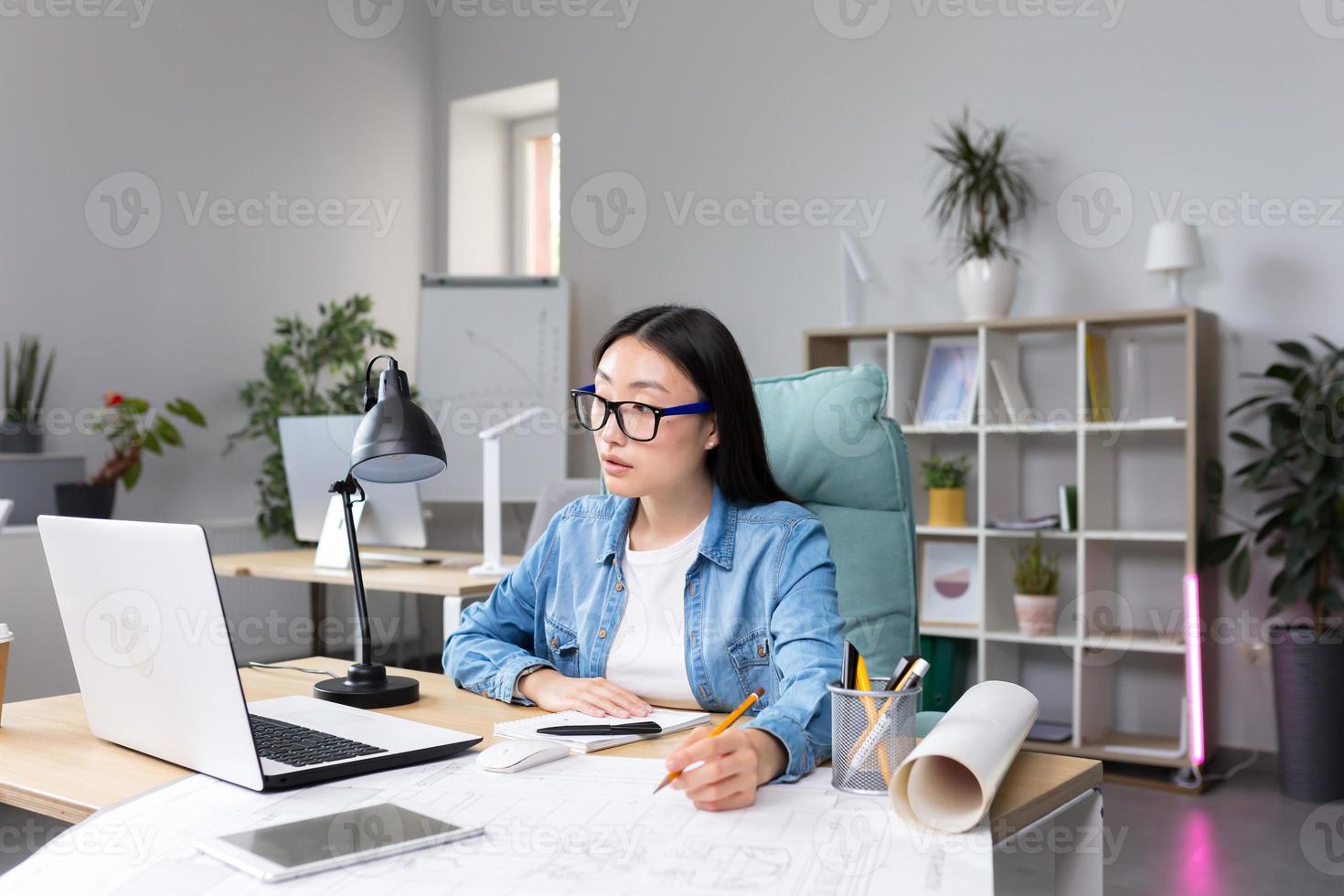 asiatisk designer arbetssätt i kontor, med ritningar, kvinna på arbete i tillfällig kläder foto
