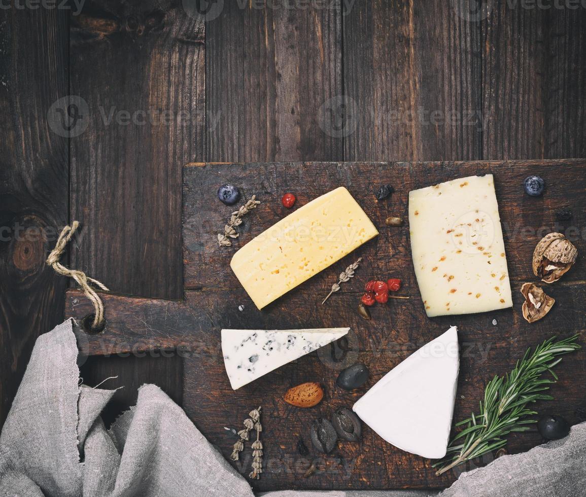 bitar av annorlunda ostar på en brun trä- styrelse brie, roquefort, ost med nötter foto