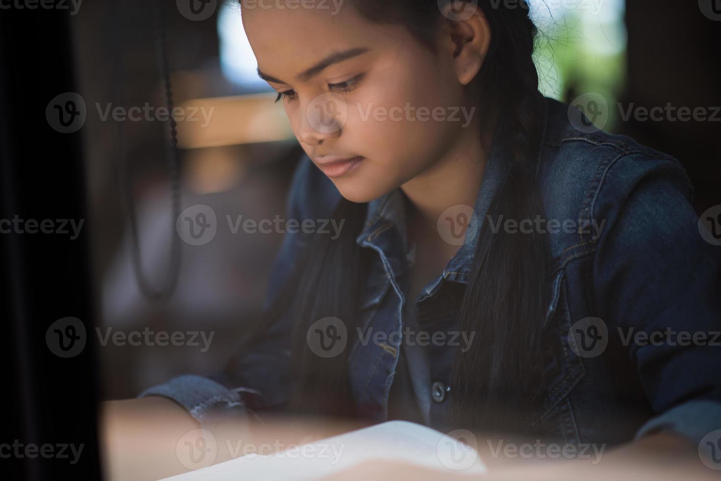 ung kvinna som läser bok sitter inomhus i ett stadscafé foto