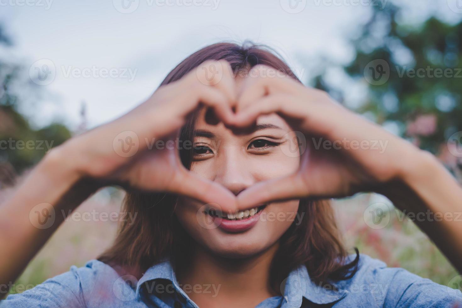 vacker kvinna ler mot kameran och gör hjärta form med händerna foto