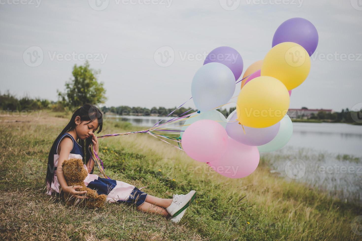 liten flicka med en nallebjörn och ballonger på ängfältet foto