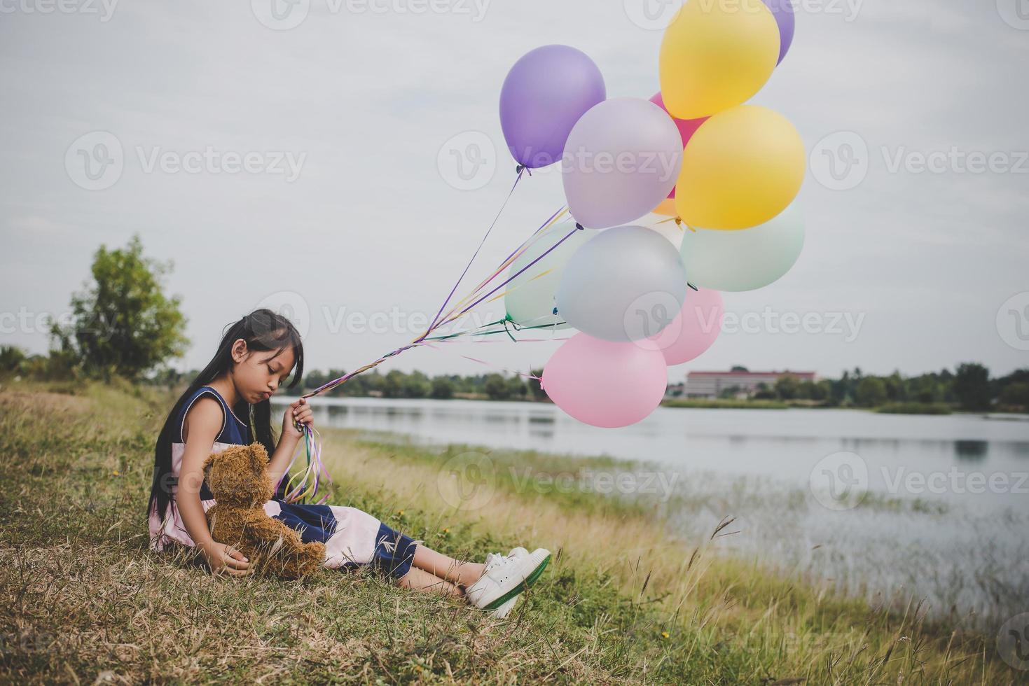 liten flicka med en nallebjörn och ballonger på ängfältet foto