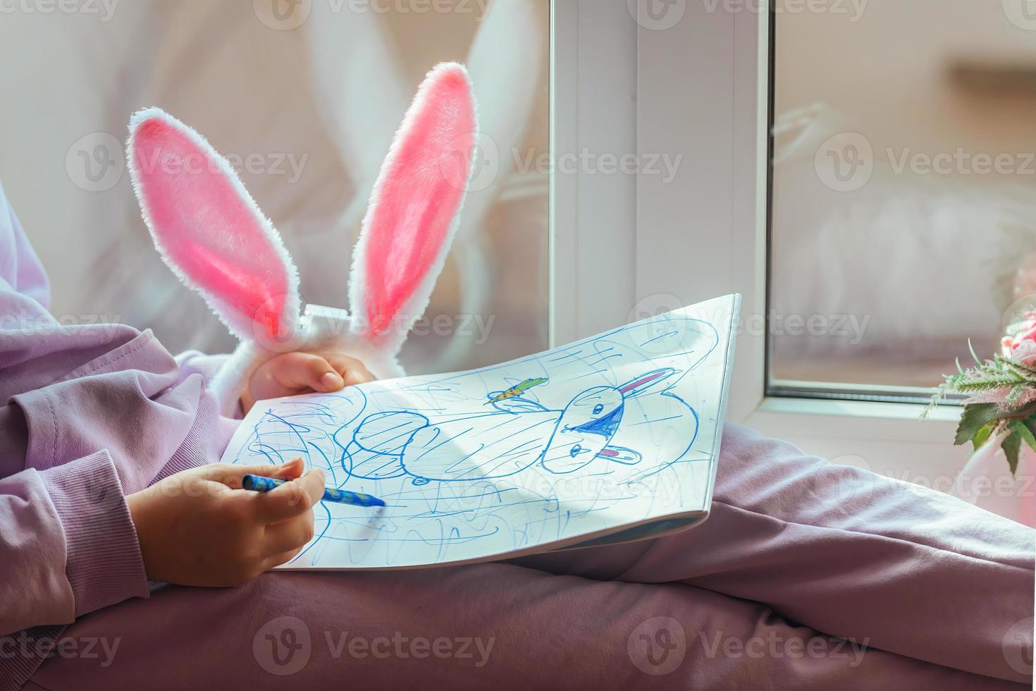en skol flicka med kanin öron sitter på de fönster och drar en kanin i henne album, framställning för påsk foto