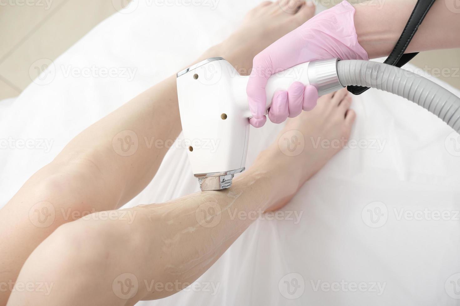 laser epilering procedur, kosmetolog rörande kvinnas ben med laser anordning. hud vård, slät och skön ben i salong. foto