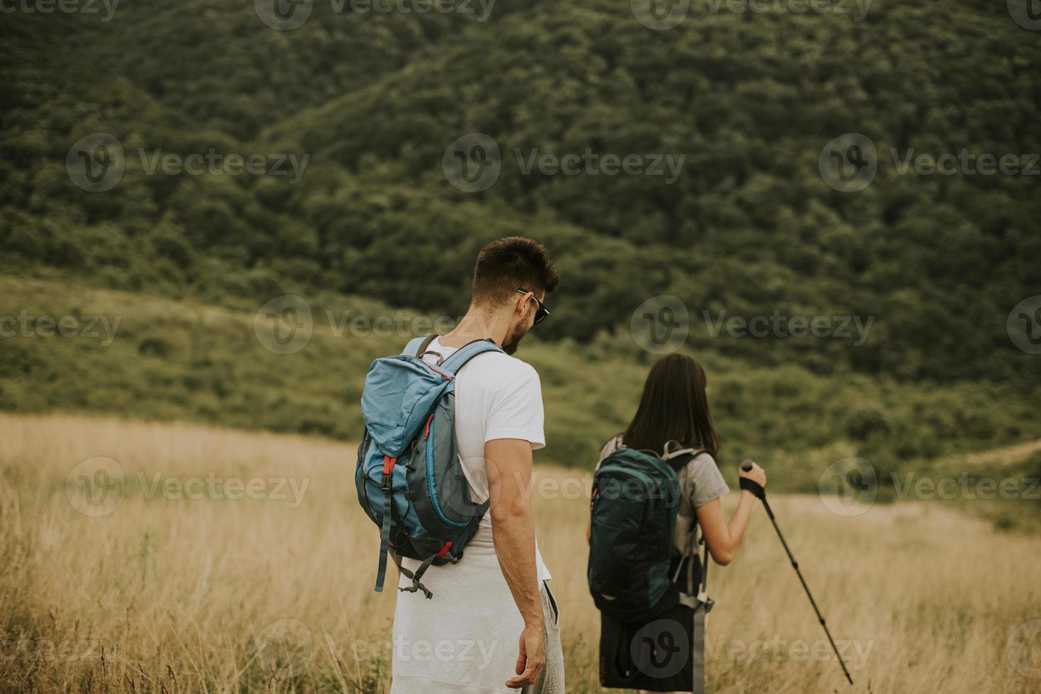 le par som går med ryggsäckar över gröna kullar foto