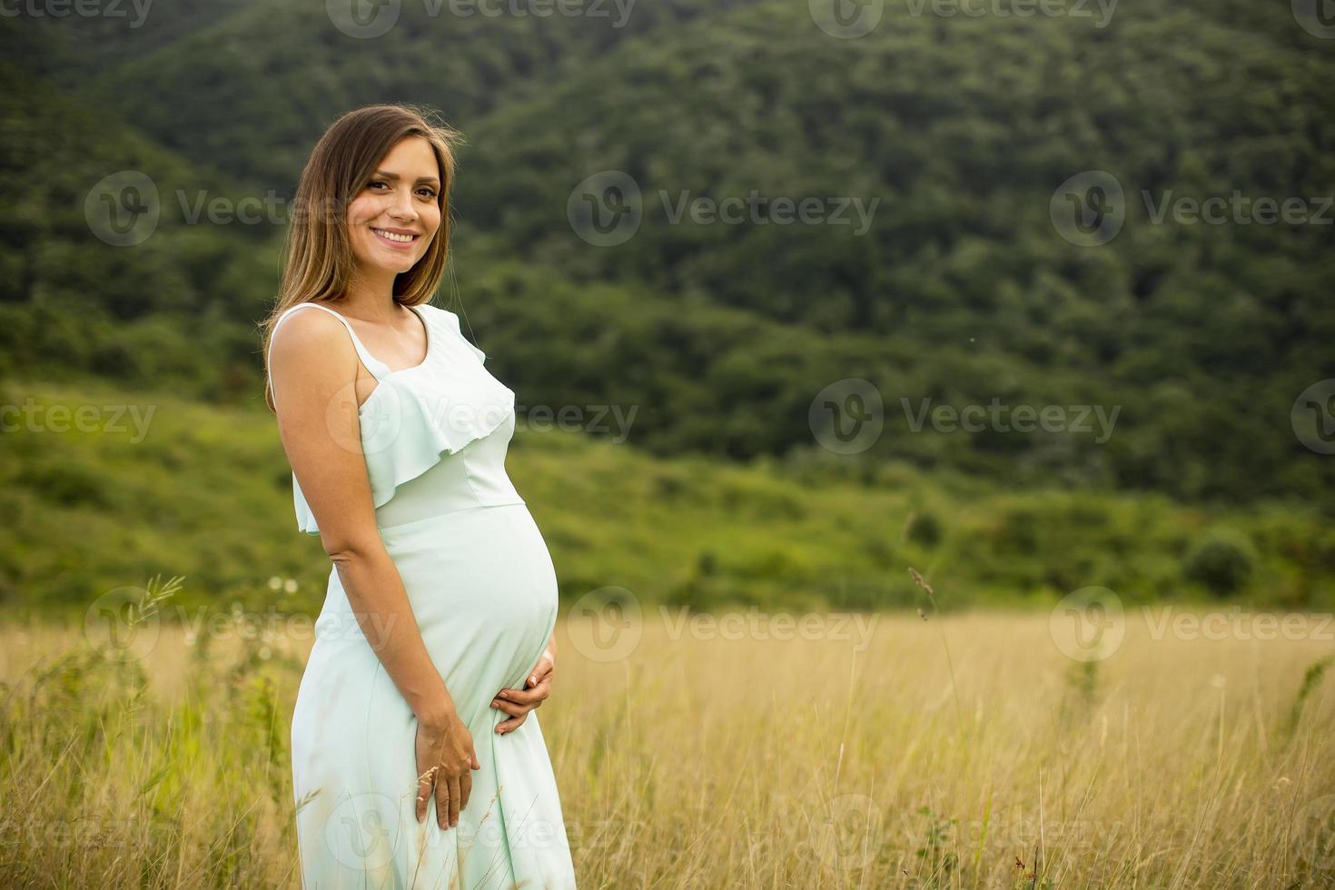 ung gravid kvinna som kopplar av utanför i naturen foto