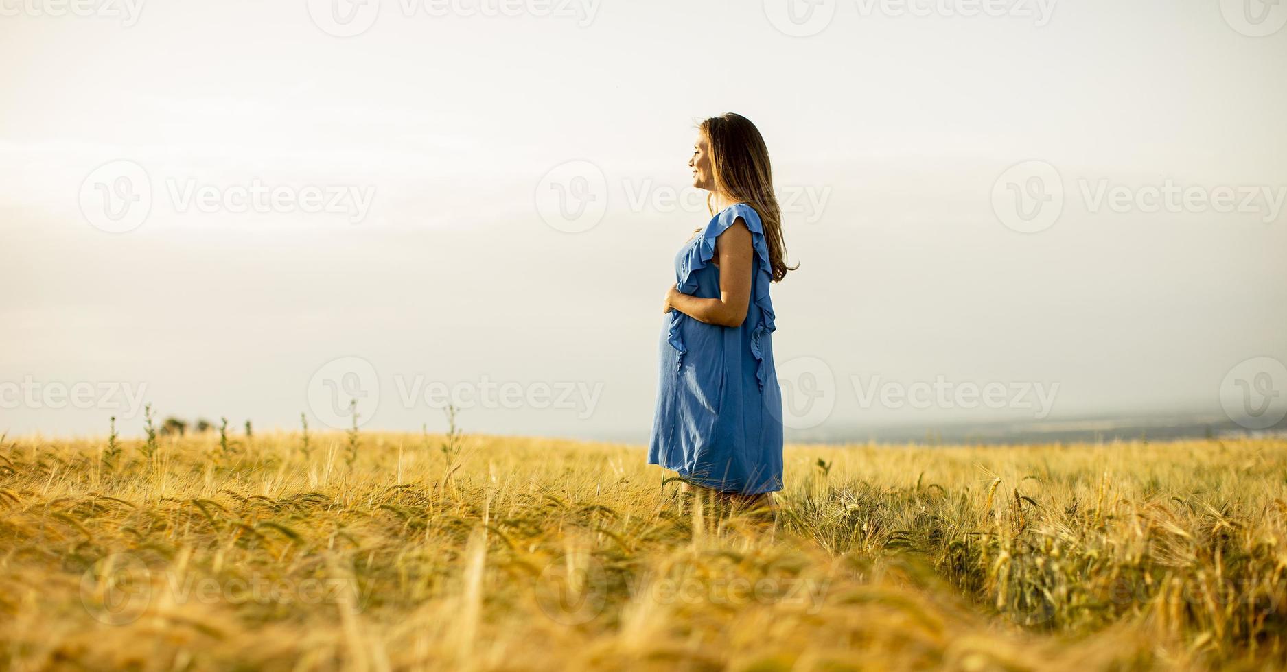 ung gravid kvinna i blå klänning som kopplar av utanför i naturen foto
