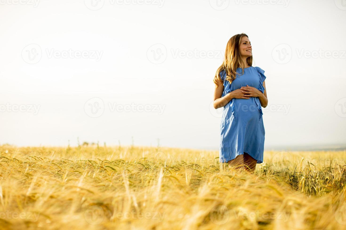 ung gravid kvinna i blå klänning som kopplar av utanför i naturen foto