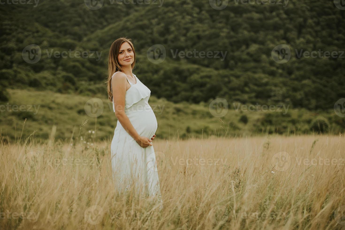 ung gravid kvinna som kopplar av utanför i naturen foto