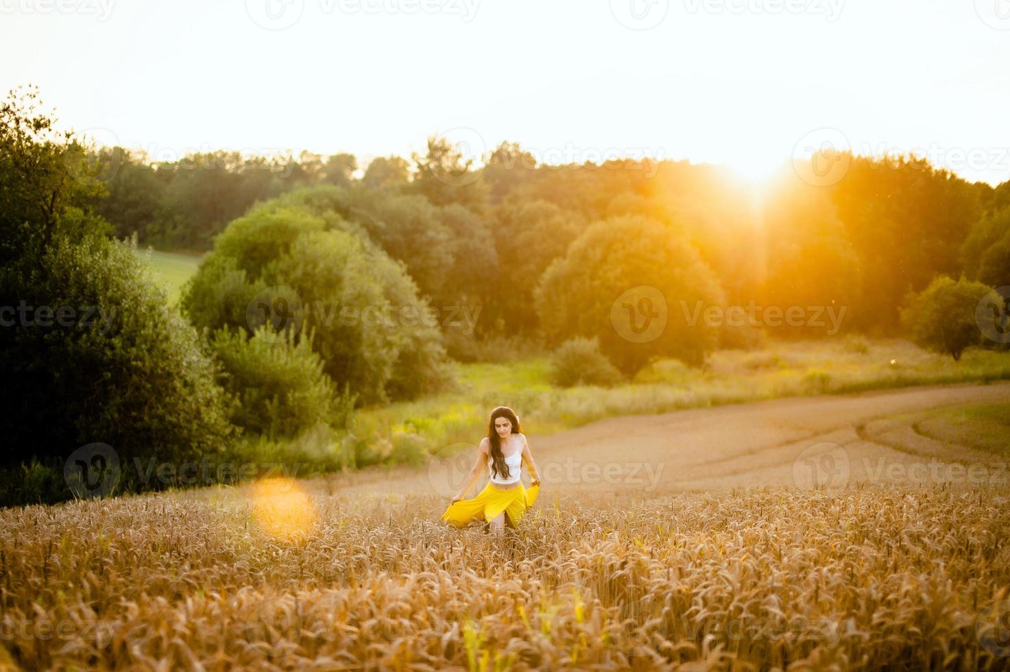 en flicka kör genom en fält med spikelets mot de bakgrund av de miljö Sol foto