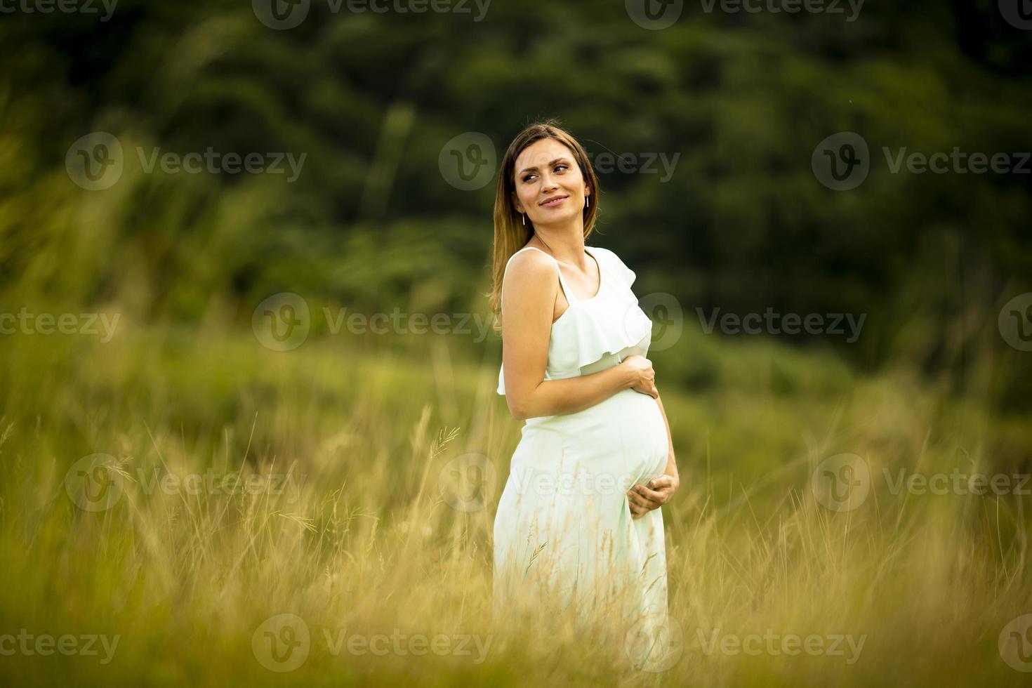 ung gravid kvinna som kopplar av utanför i naturen foto