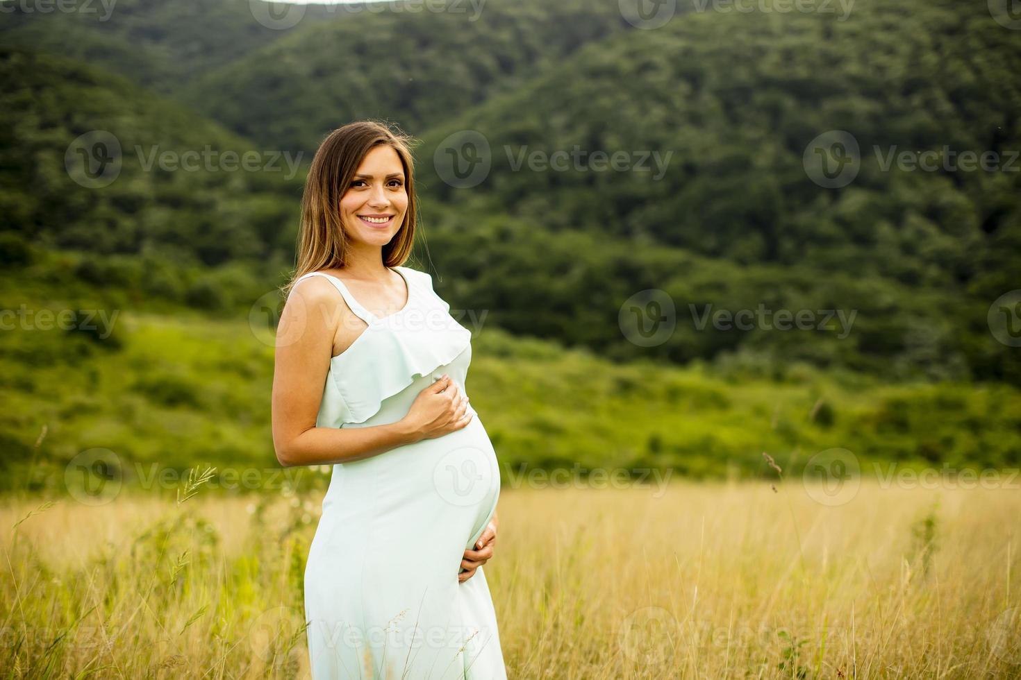 ung gravid kvinna som kopplar av utanför i naturen foto