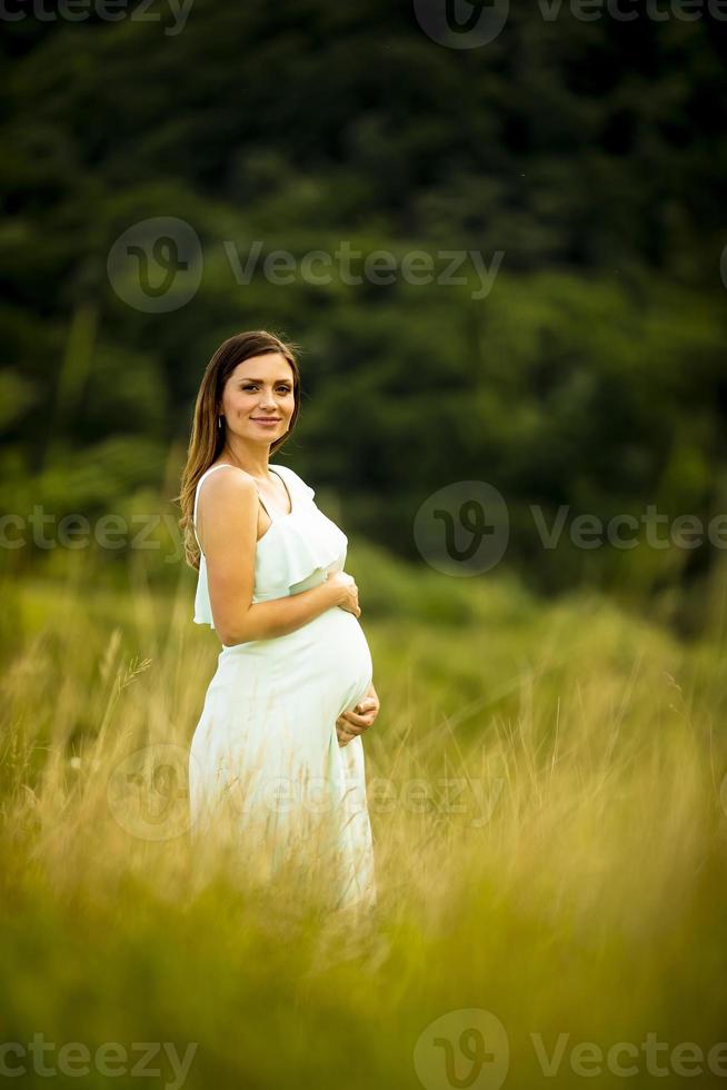 ung gravid kvinna som kopplar av utanför i naturen foto