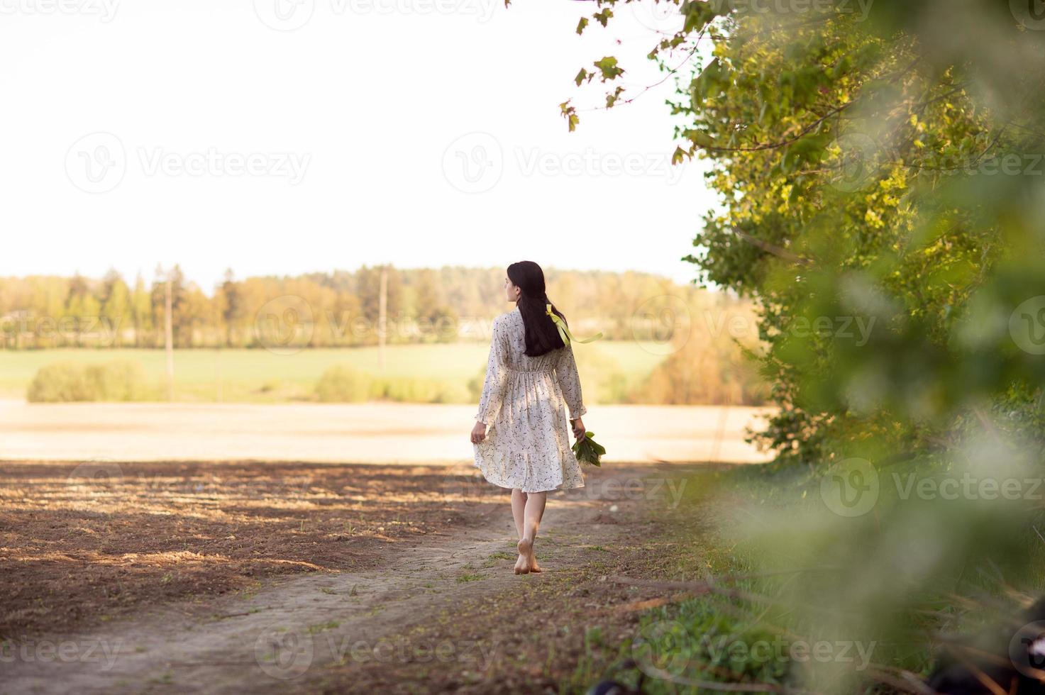 en söt flicka i en vit lång klänning står i vår på en gul rapsfrö fält foto