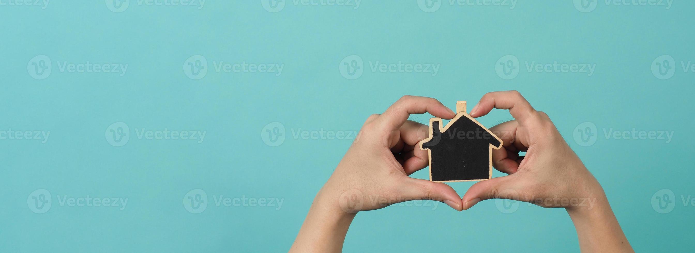 små trä hus i händer representera begrepp sådan som Hem vård familj kärlek verklig egendom hus skydd försäkring och inteckning. händer innehav små modell hus isolerat på blå grön studio bakgrund. foto