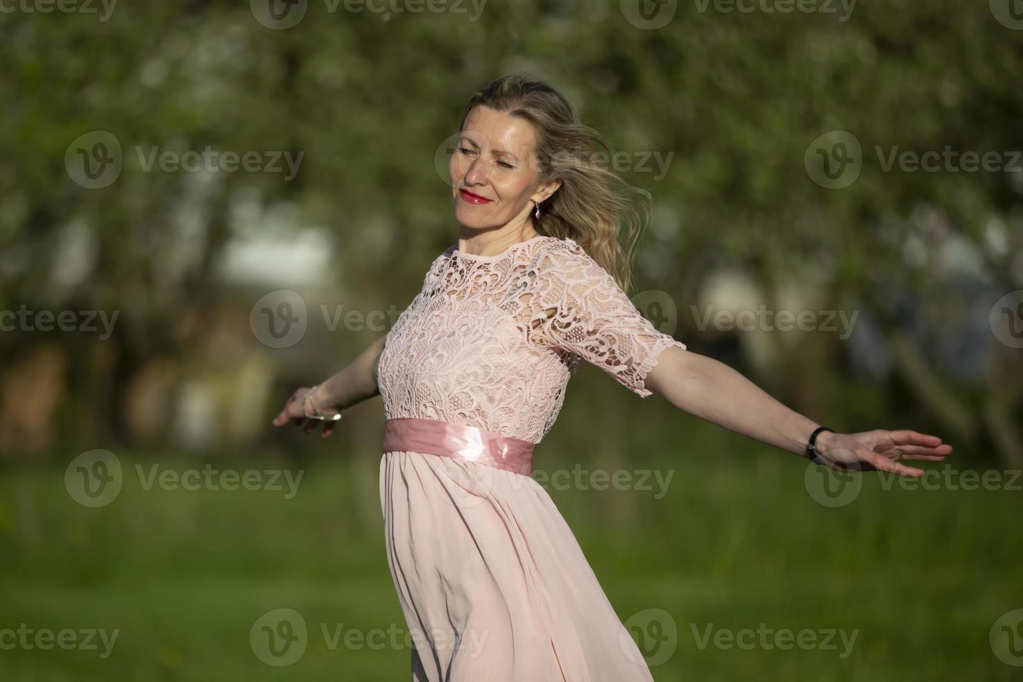 en skön äldre blond kvinna i en romantisk klänning öppnad henne vapen och åtnjuter de vind. foto