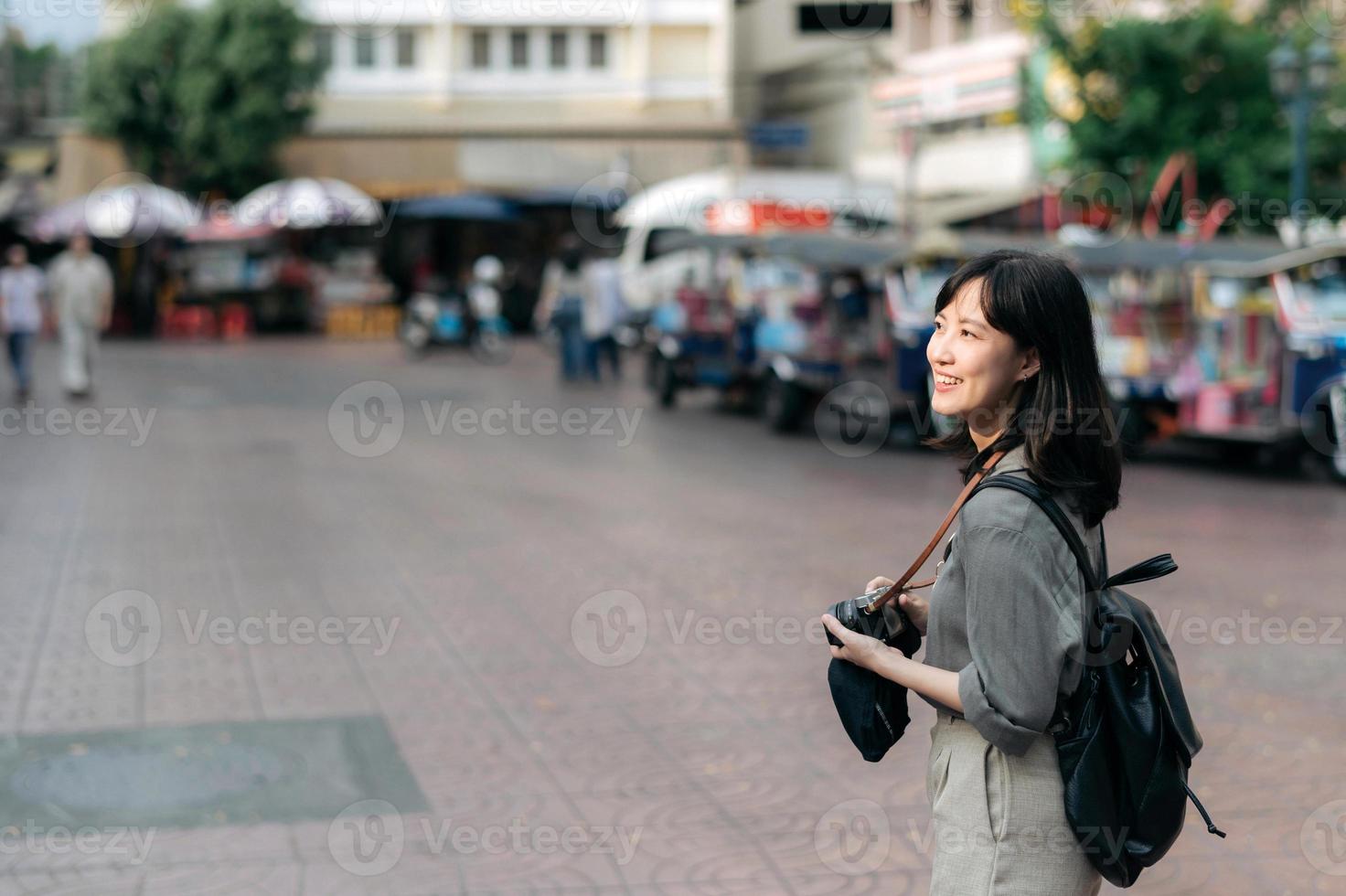 ung asiatisk kvinna ryggsäck resande använder sig av digital kompakt kamera, njuter gata kulturell lokal- plats och leende. resande kontroll ut sida gator. foto