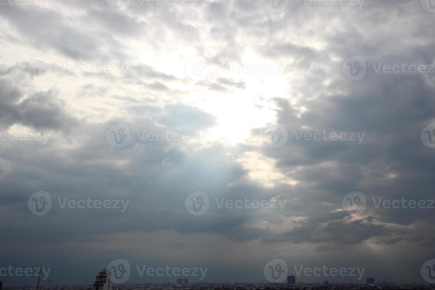 solnedgång himmel ovan tung mörk moln nästan regnar med dramatisk strålar av ljus lysande ner bakgrund och stad kväll tid foto