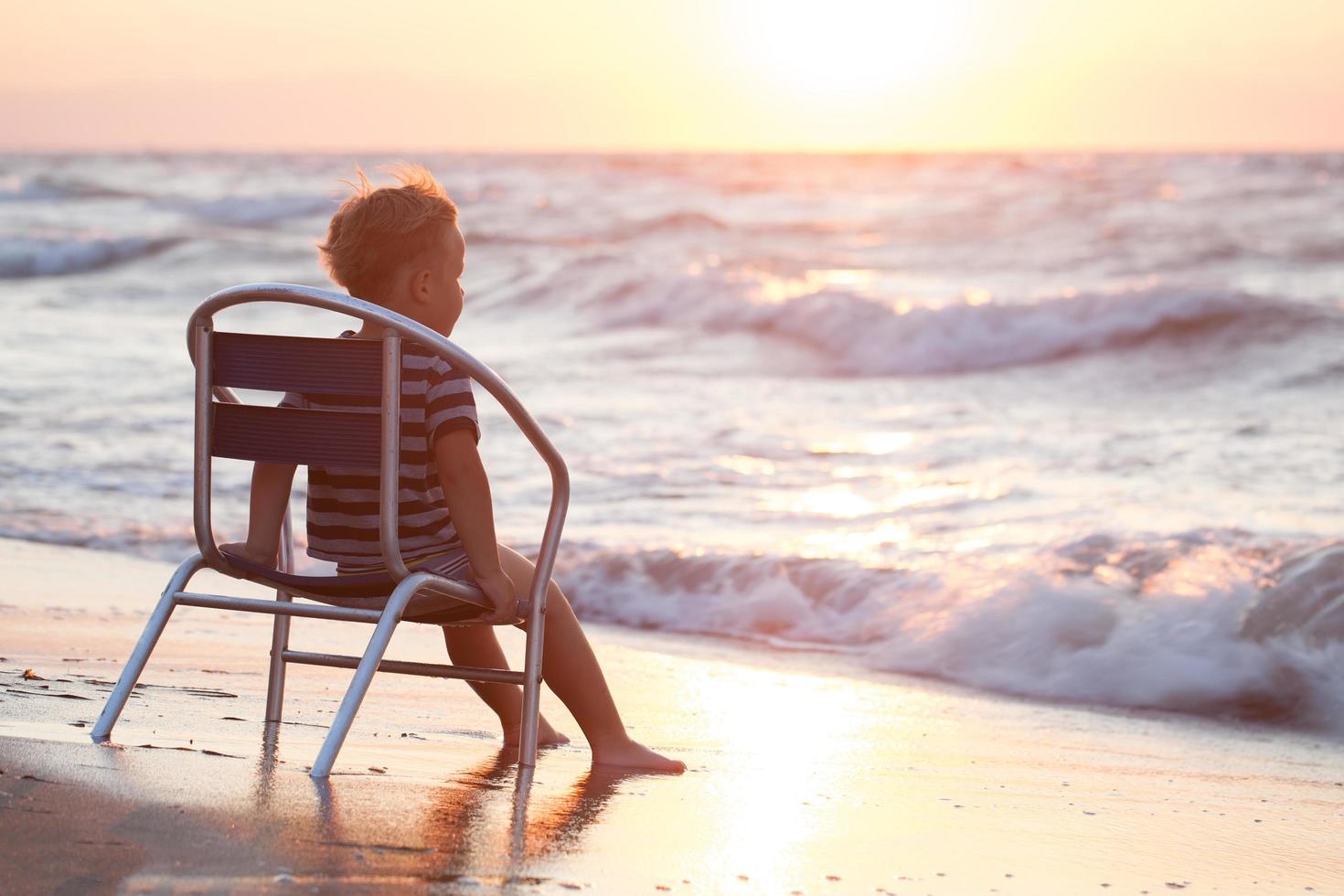 pojke sitter på en stol vid havet foto