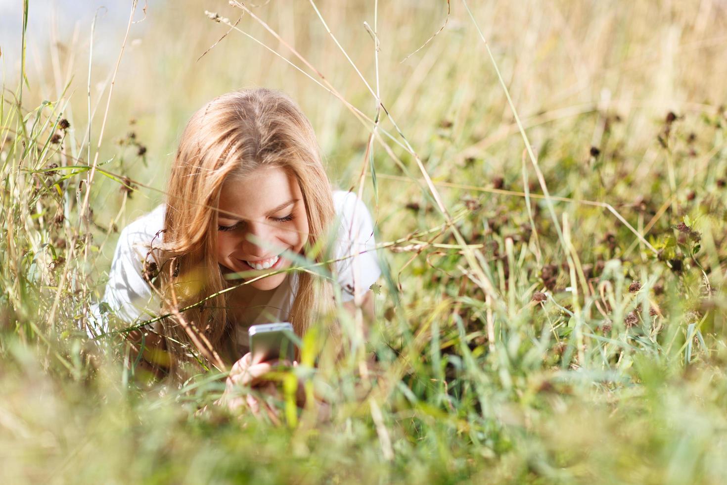flicka med en telefon som lägger i gräset foto