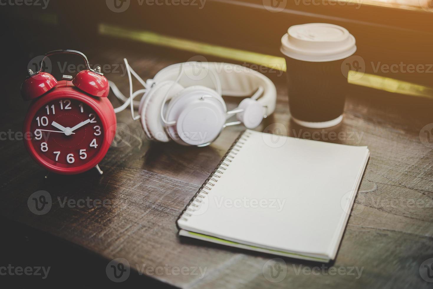 kopp kaffe, anteckningsbok och röd väckarklocka med hörlurar på ett träbord foto