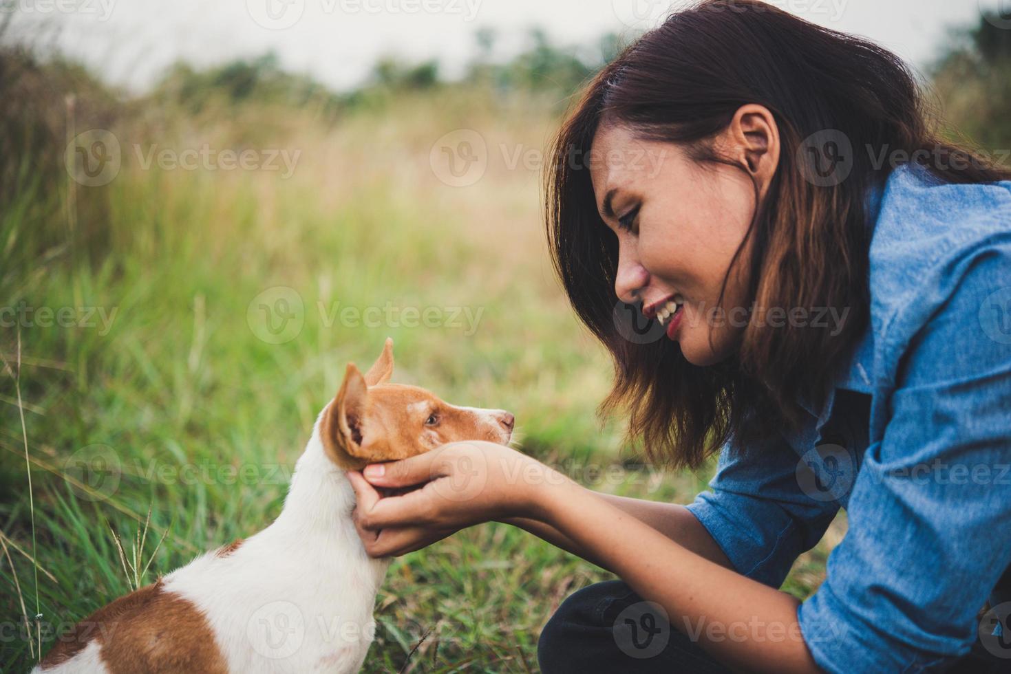 glad glad hipsterflicka som leker med sin hund i parken under solnedgången foto