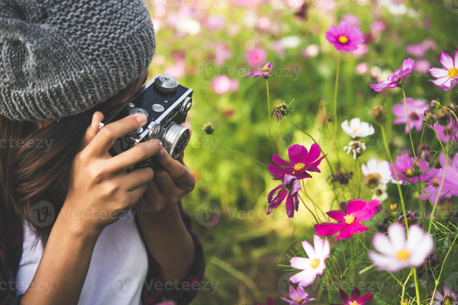 hipster tjej med vintage kamera fokus skytte blommor i en trädgård foto