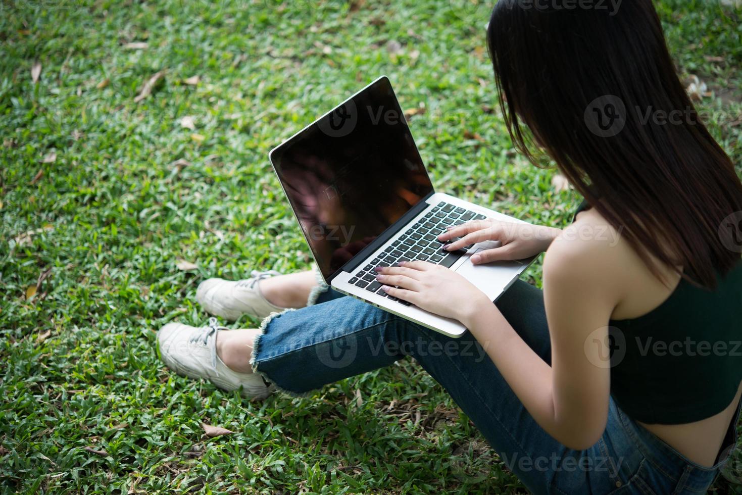 ung vacker kvinna som sitter på grönt gräs och använder bärbar dator i parken foto