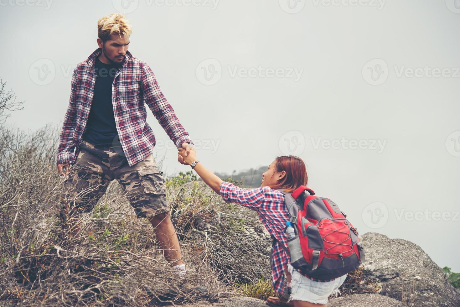 ung hipster man hjälper kvinnan klättra berg foto