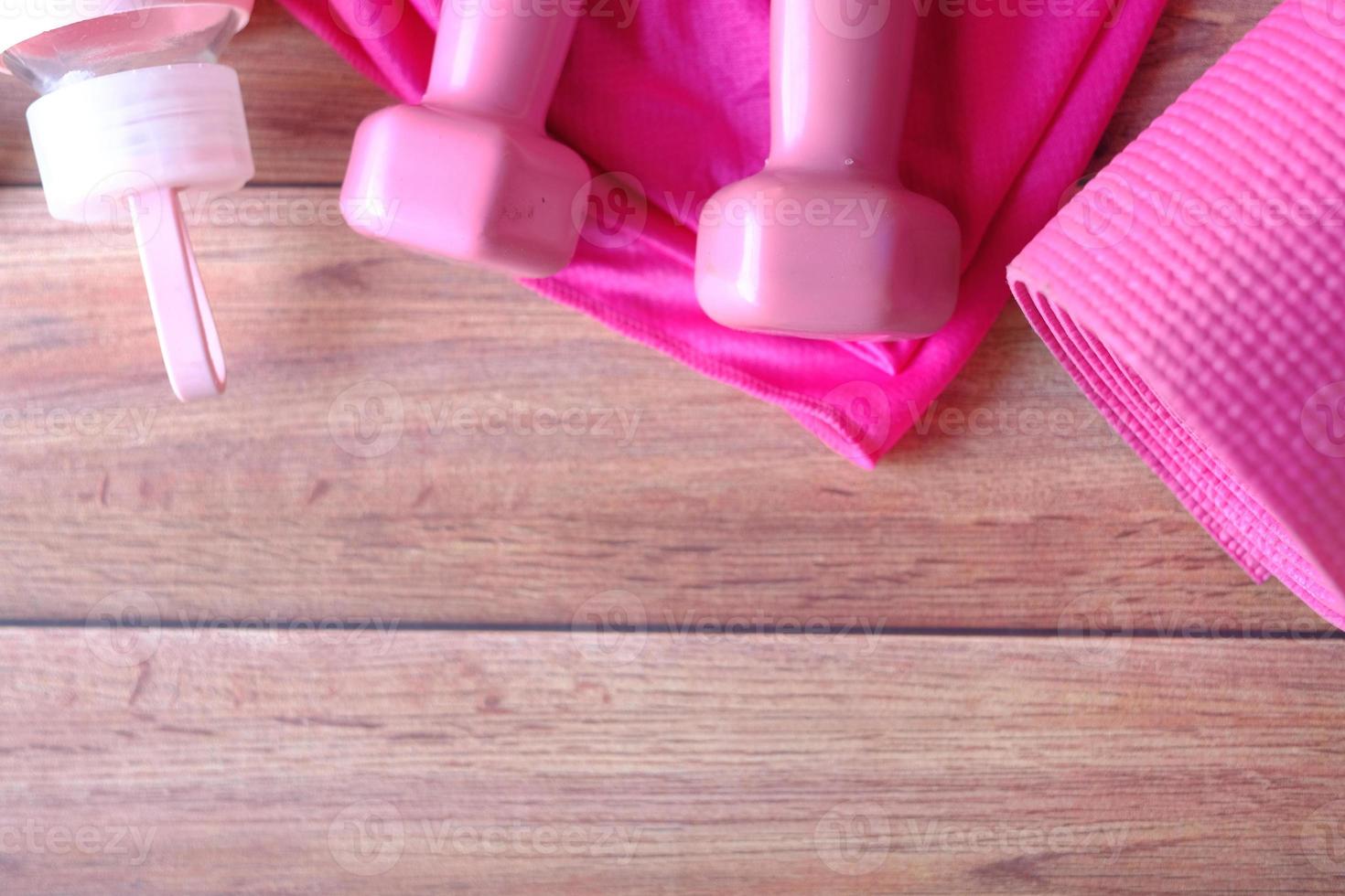 rosa färgad hantel, träningsmatta och vattenflaska på träbakgrund foto