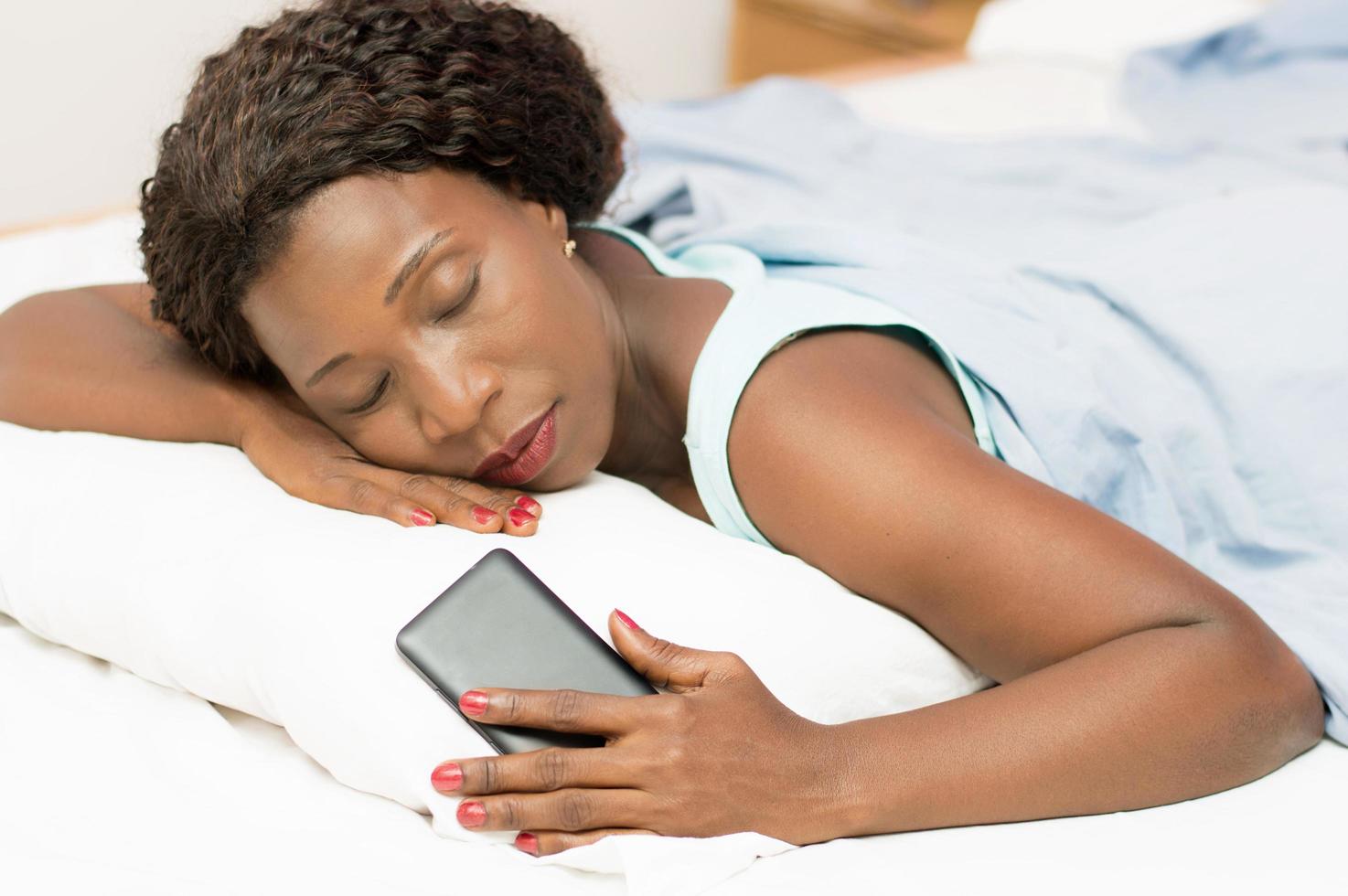 vacker kvinna som sover i sängen med telefonen i handen foto