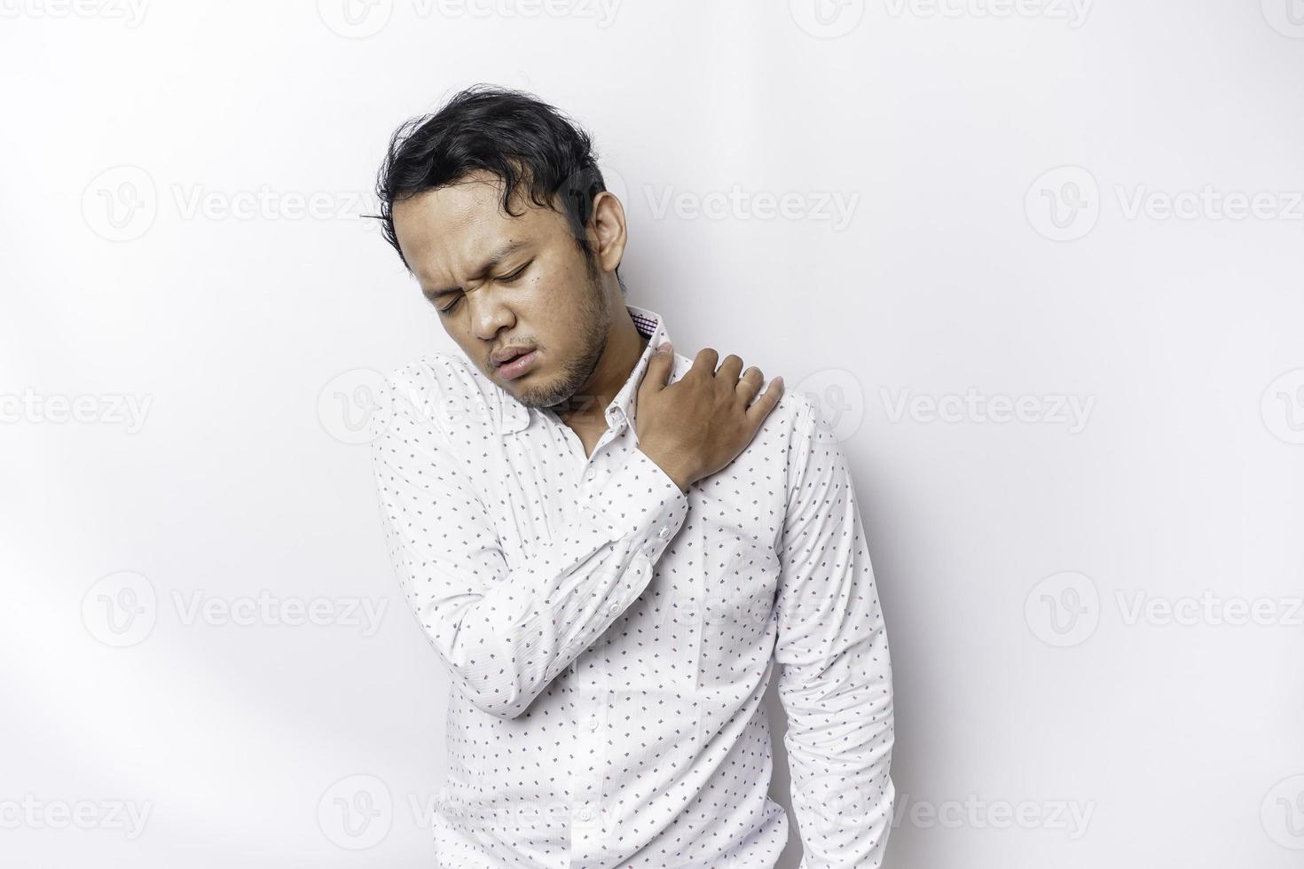 trött upprörd ung man bär vit skjorta lidande från smärta, muskel spasm på arbetsplats. Trötthet, deadline, smärta och felaktig hållning foto