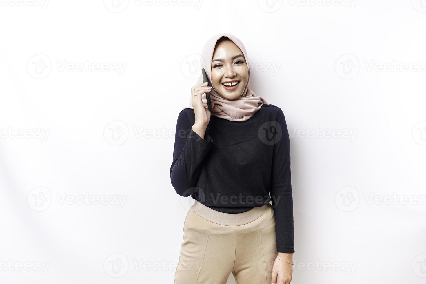 en porträtt av en Lycklig asiatisk muslim kvinna bär en hijab, innehav henne telefon, isolerat förbi vit bakgrund foto