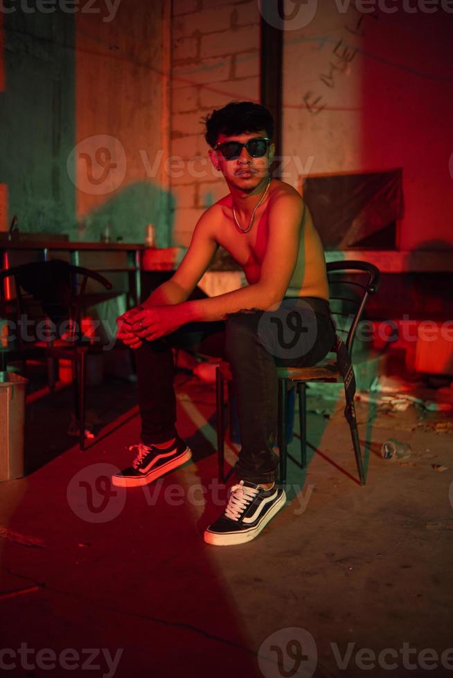 en Gay man i solglasögon och denim byxor sitter avkopplande i en klubb till fira foto