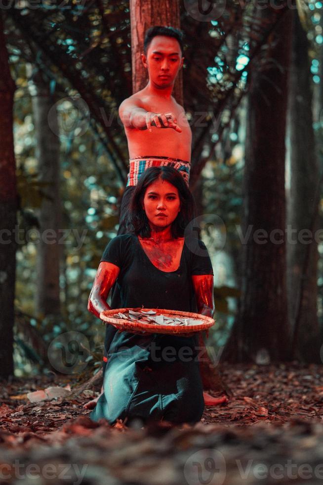 ett asiatisk kvinna och man var stående i främre av en träd medan jakt ett djur- i de mitten av de skog fram tills de var täckt i blod foto