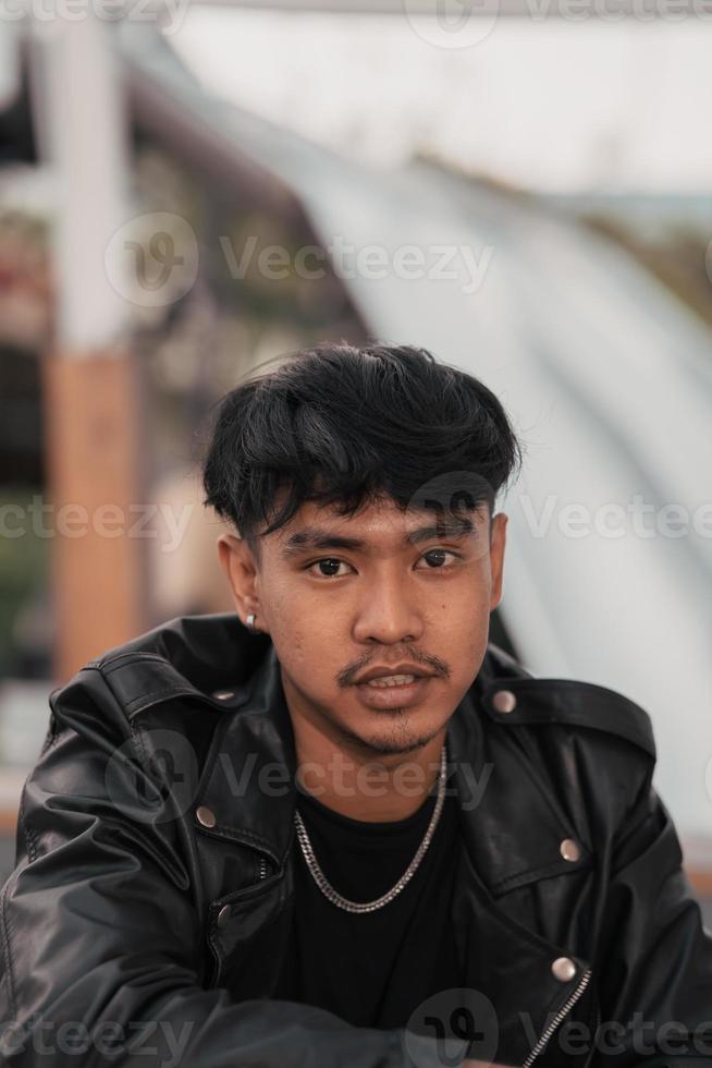 ett asiatisk man med en stygg ansikte bär en kedja halsband och en svart läder jacka i en Kafé foto